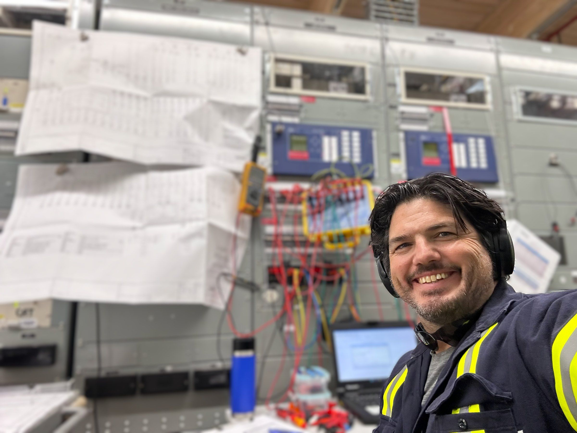 Jeff Burkinshaw smiling in hi-vis gear in front of relay panels he is testing